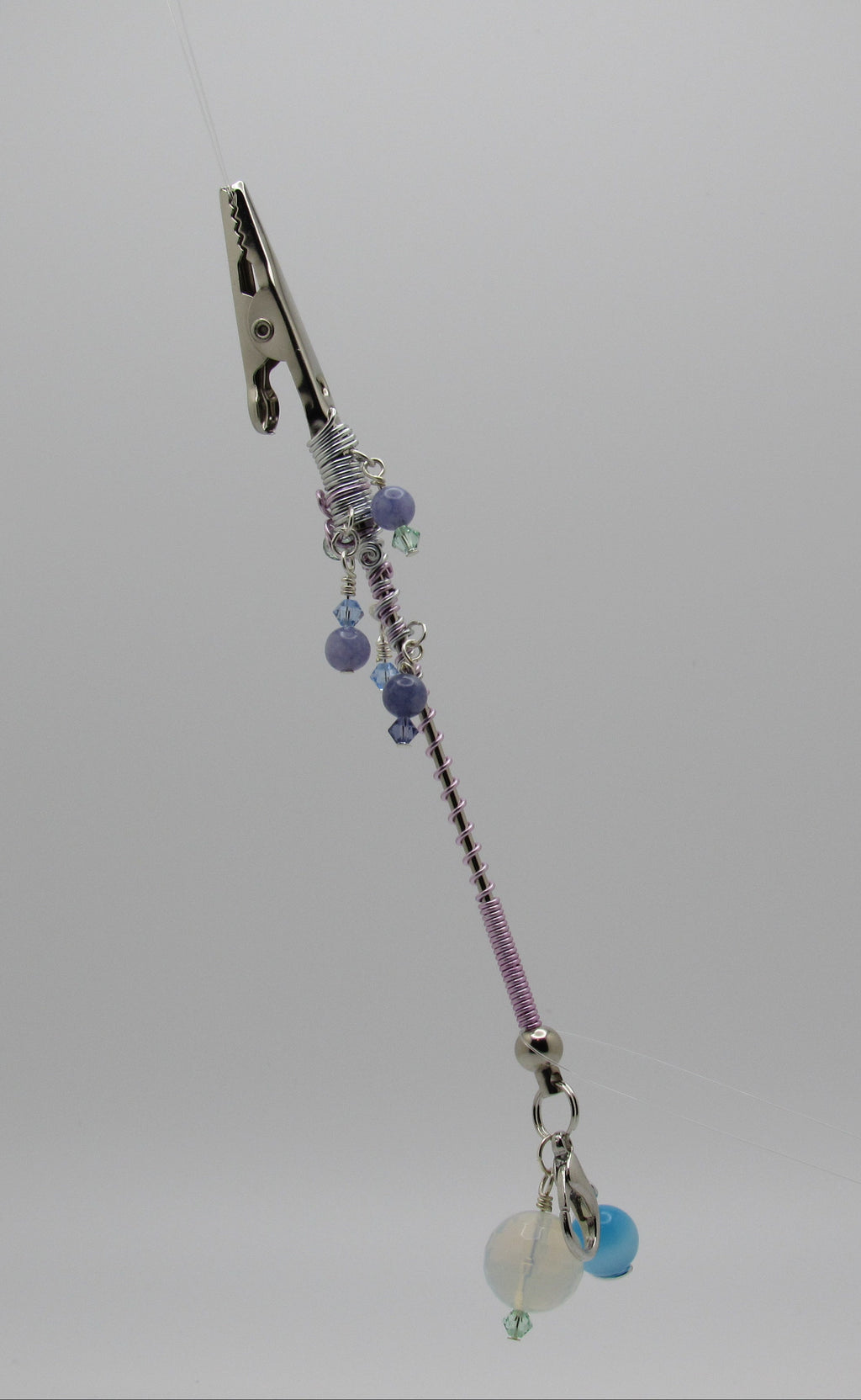 A beaded accessory with a silver metal clip at the top, purple and silver beads, and small dangling charms, shown against a plain light gray background.