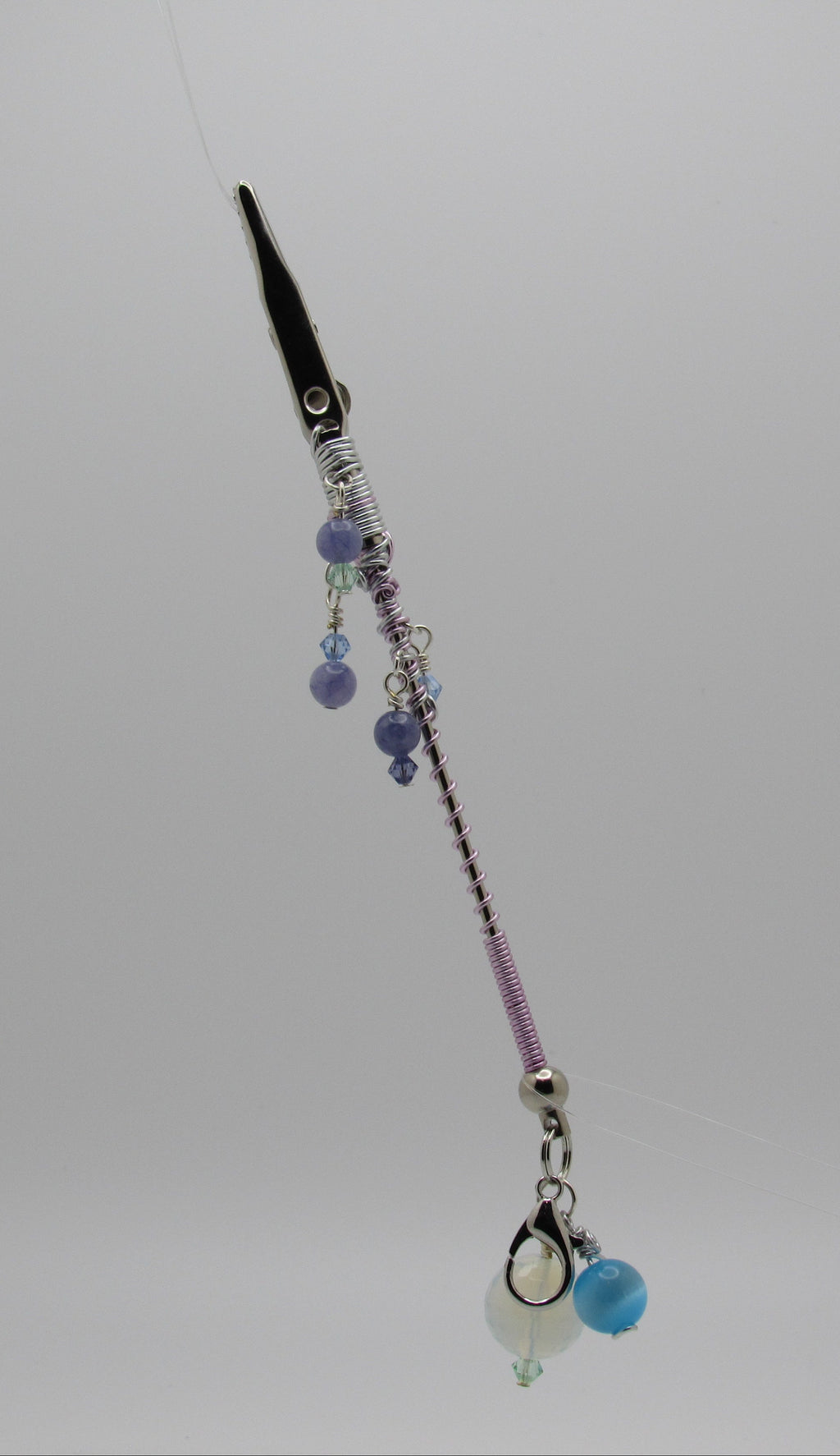 Silver roach clip with silver  and lavender metal wire, purple and blue beads, and a small white bead charm, shown against a plain light gray background.