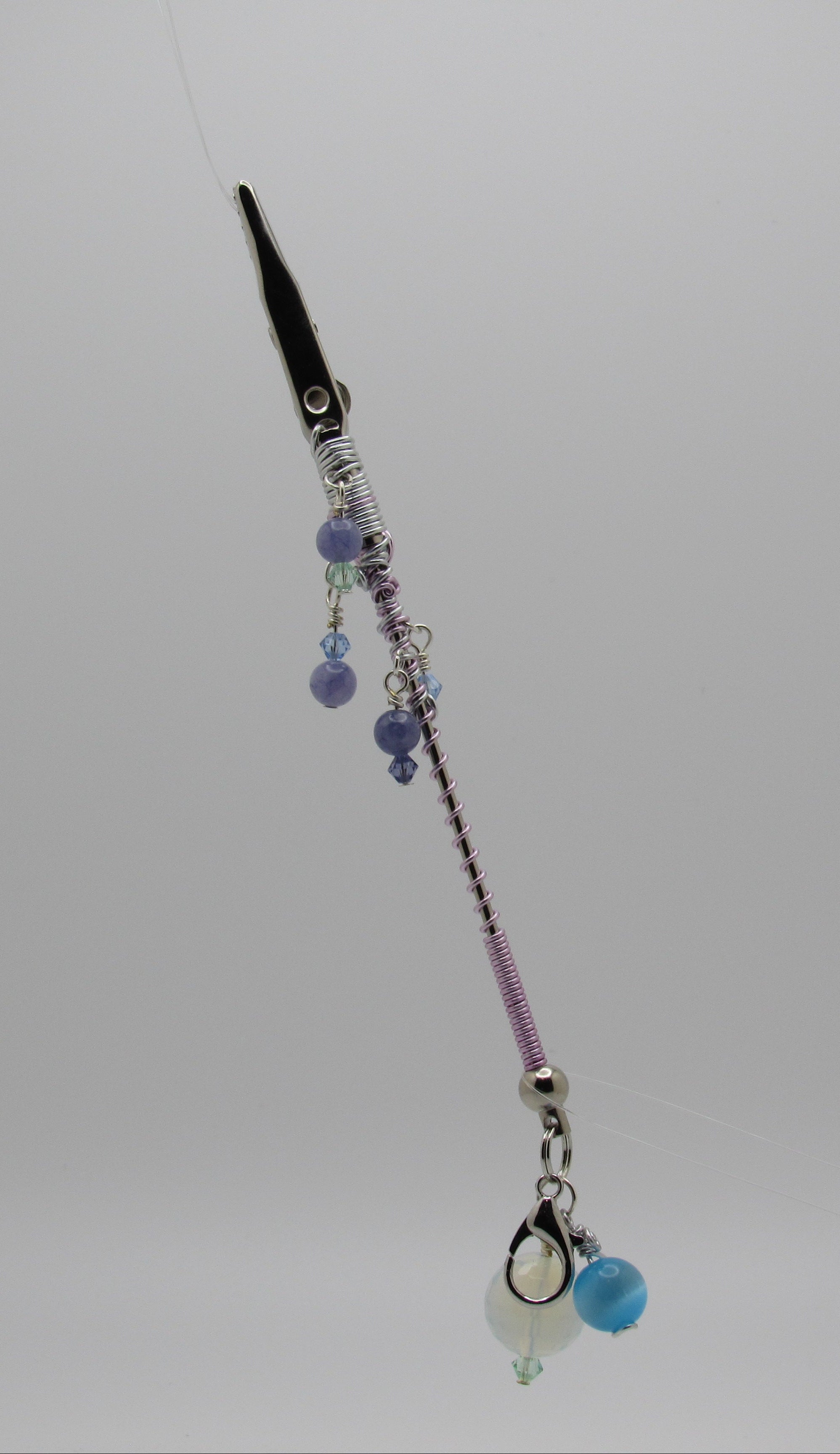 Silver roach clip with silver  and lavender metal wire, purple and blue beads, and a small white bead charm, shown against a plain light gray background.