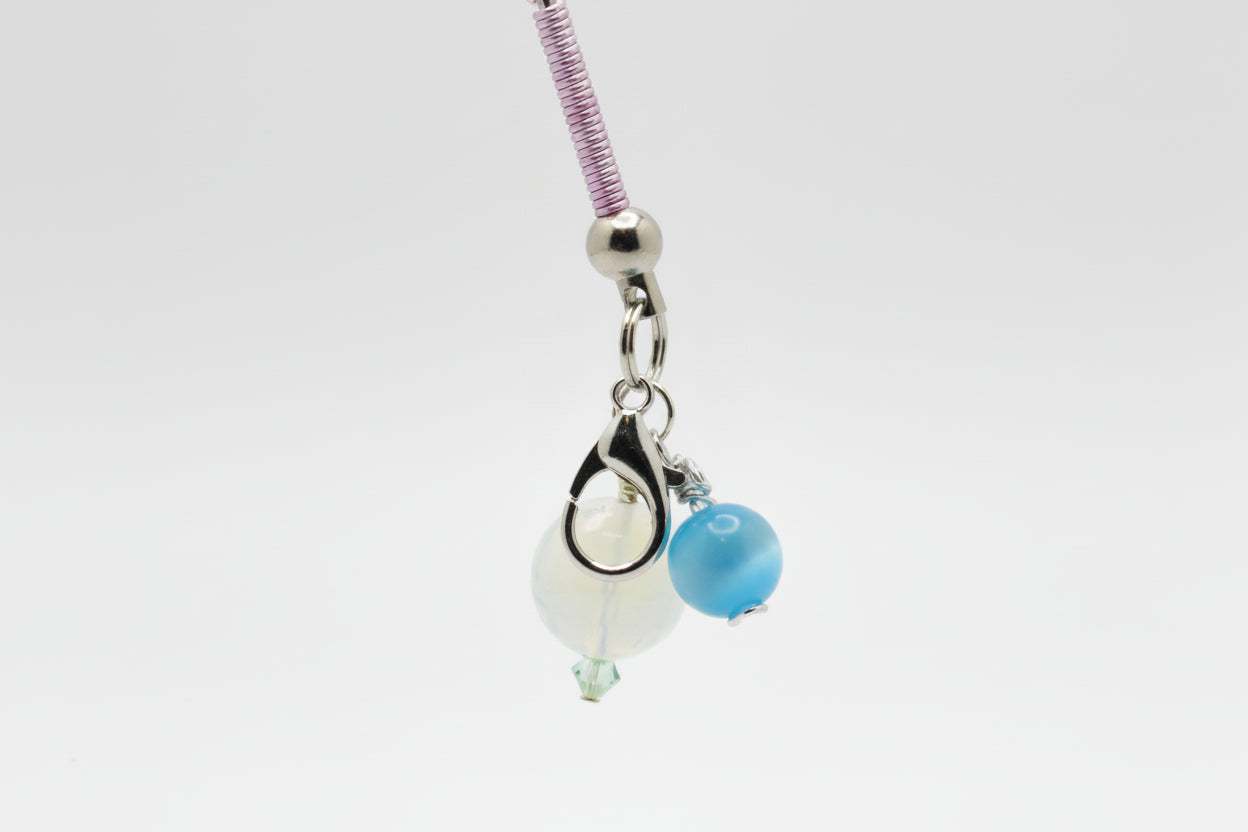 A close-up roach clip base with a silver lobster clasp, a white bead, a blue bead, and a purple wire wrapped on silver post on a neutral gray background.