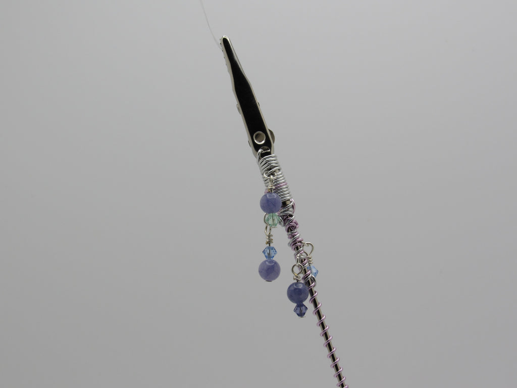 A close-up of top of clip, silver wire wrapping, and dangling purple beads on a gray background.