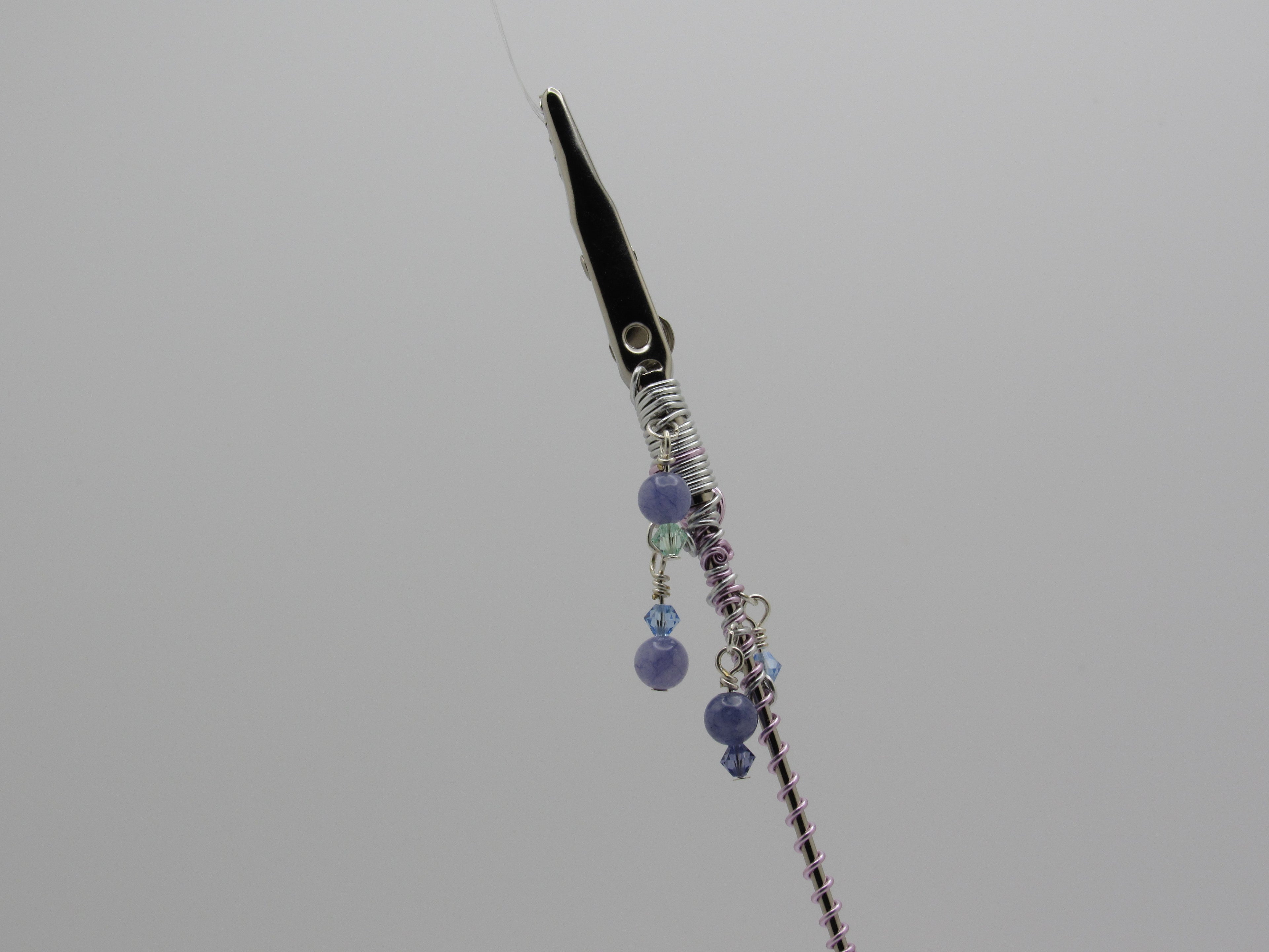 A close-up of top of clip, silver wire wrapping, and dangling purple beads on a gray background.