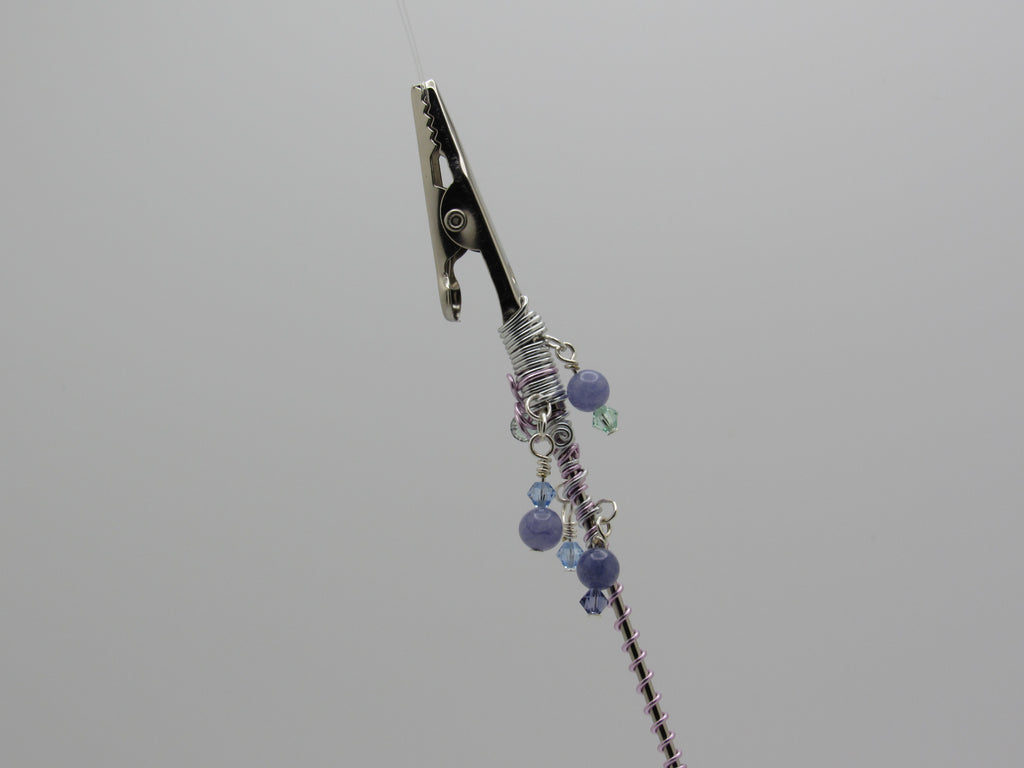 A close-up of clip at the top and a wrapped section decorated with purple and blue beads, set against a solid gray background.
