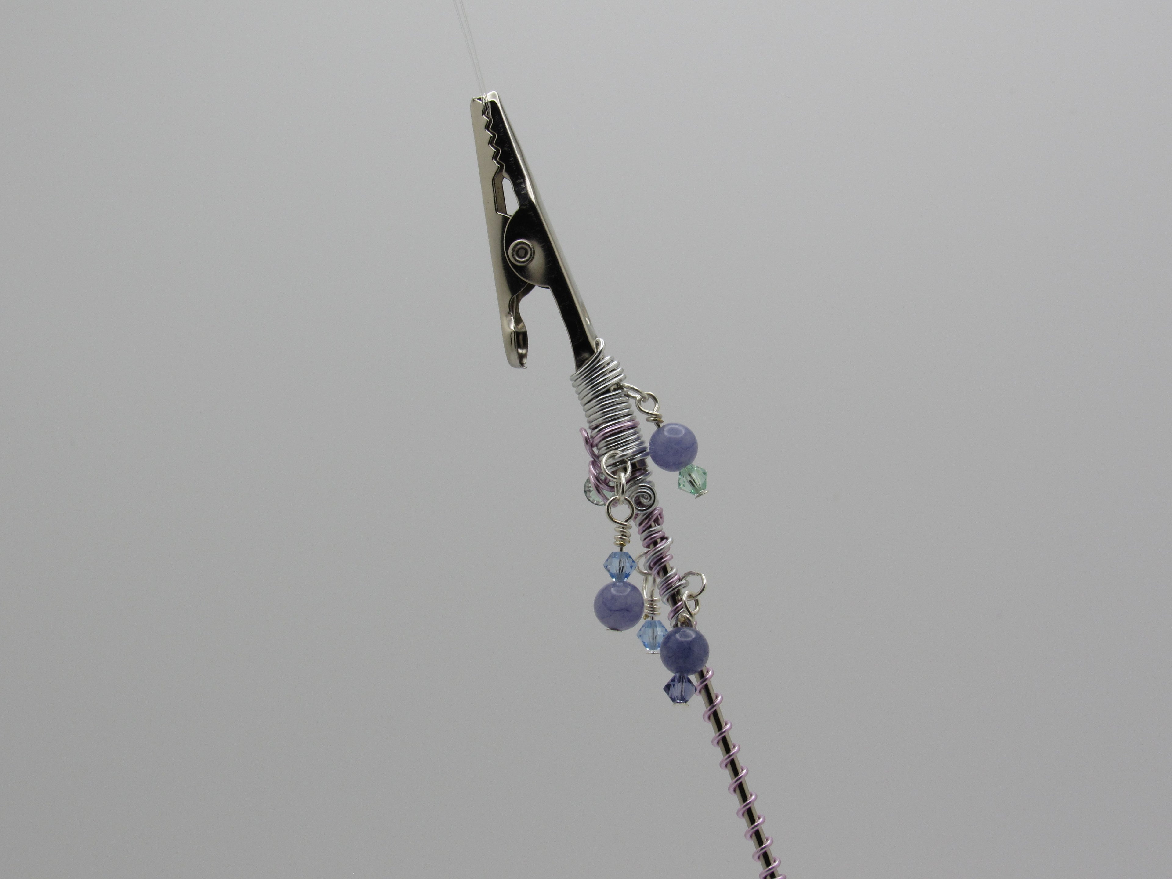 A close-up of clip at the top and a wrapped section decorated with purple and blue beads, set against a solid gray background.
